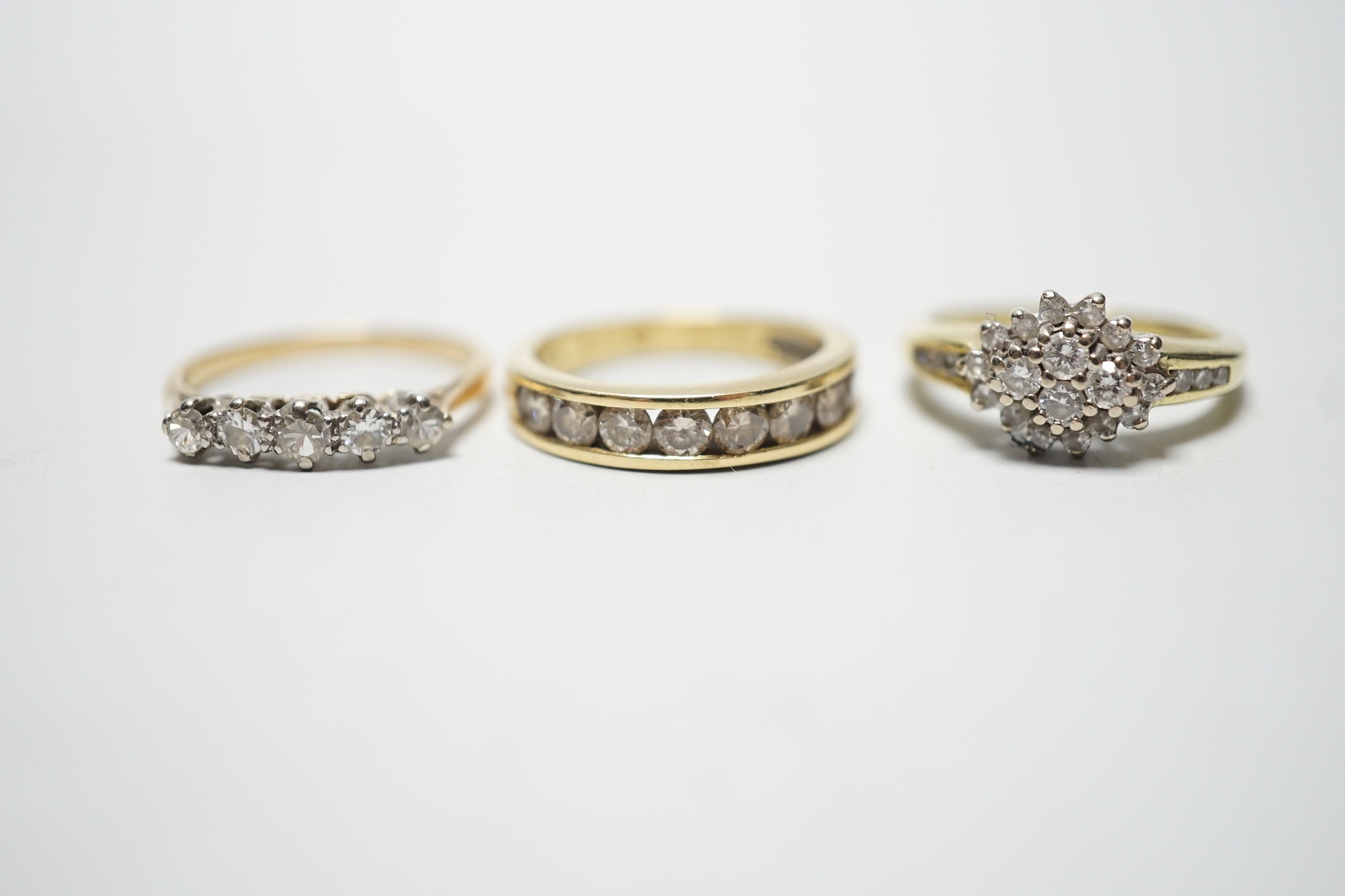 Two modern 18ct gold and diamond set rings, including nine stone channel set, size L and diamond cluster, size L and a yellow metal and five stone diamond set half hoop ring, size M, gross weight 9 grams.